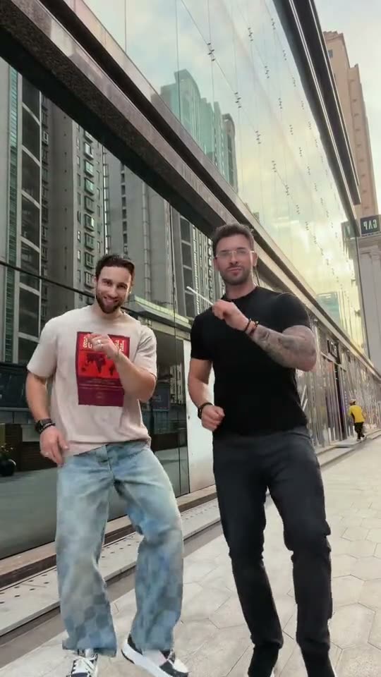 Abra Kadabra trend: a man in black starts the hand dance, then his friend in a white T-shirt appears beside him outdoors