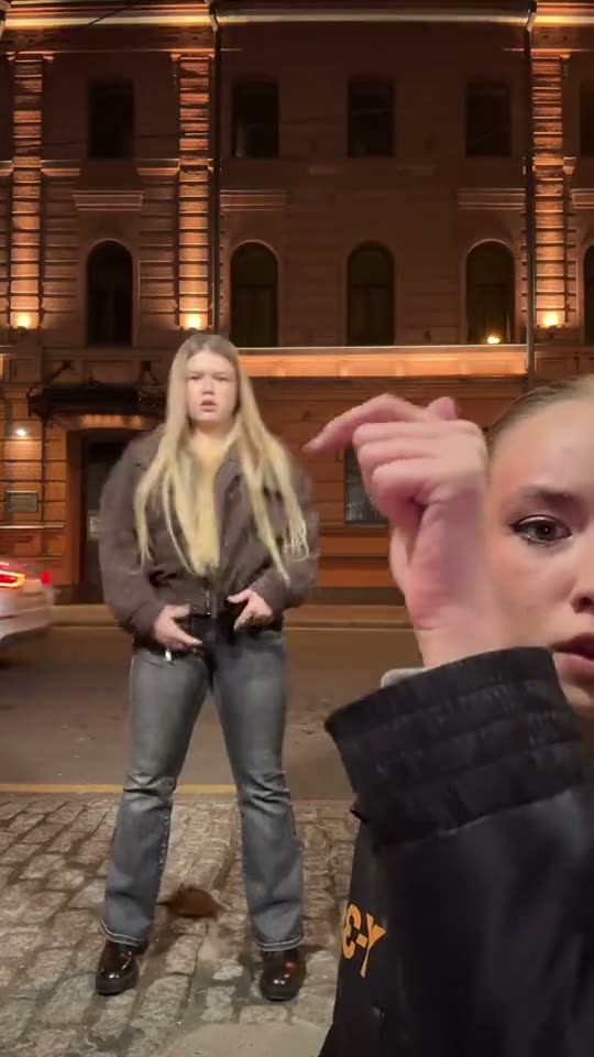 Hop hop hop dance: two friends in jackets squish each other in a lit city square at night