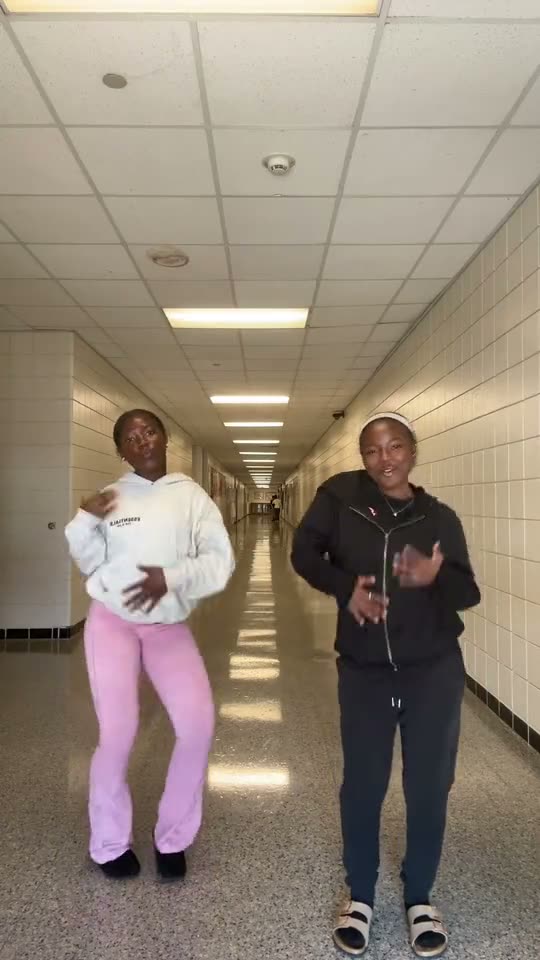 Puerto Rican mami dance: two friends in a white hoodie and pink trousers and in black do the dance in a school hallway