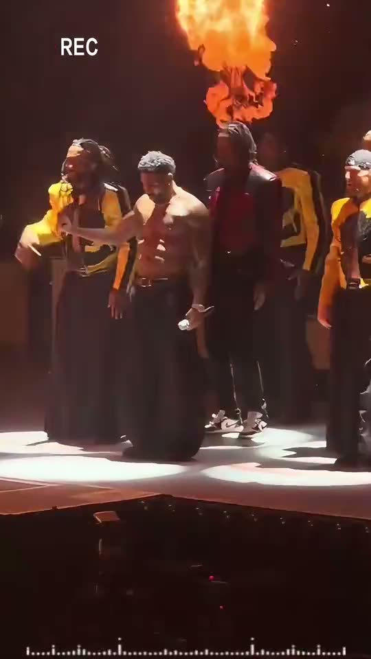 Talk Dirty dance AI: a shirtless lead in baggy trousers dances in the spotlight as the fire jets roar behind the crew